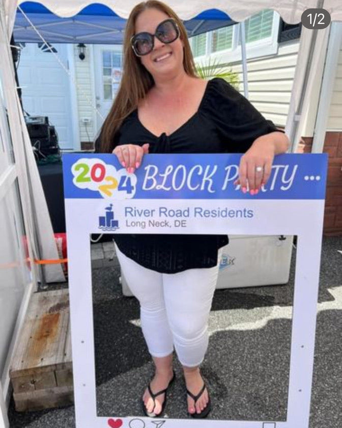 Woman holding a '2024 Block Party' sign at an outdoor event.