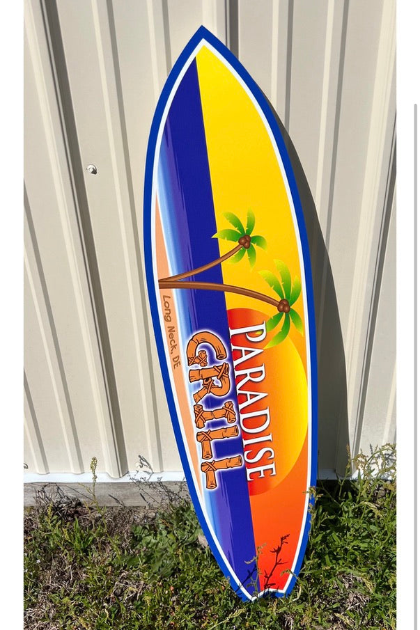 Colorful surfboard-shaped sign with 'Paradise Grill' branding on a grassy background.
